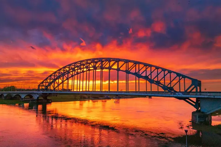 Stahlbogenbrücke über einen Fluss bei leuchtend rotem Sonnenuntergang